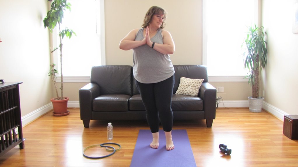 A woman stands on a yoga mat in a living room, hands pressed together in front of her chest. Exercise equipment, a water bottle, and a ring lie nearby—perfect for anyone seeking belly fat reduction or looking for flat stomach tips at home.